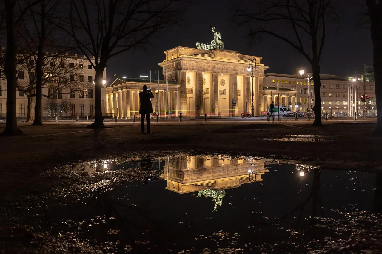 The Brandenburg Gate lit at night, reflected in a puddle