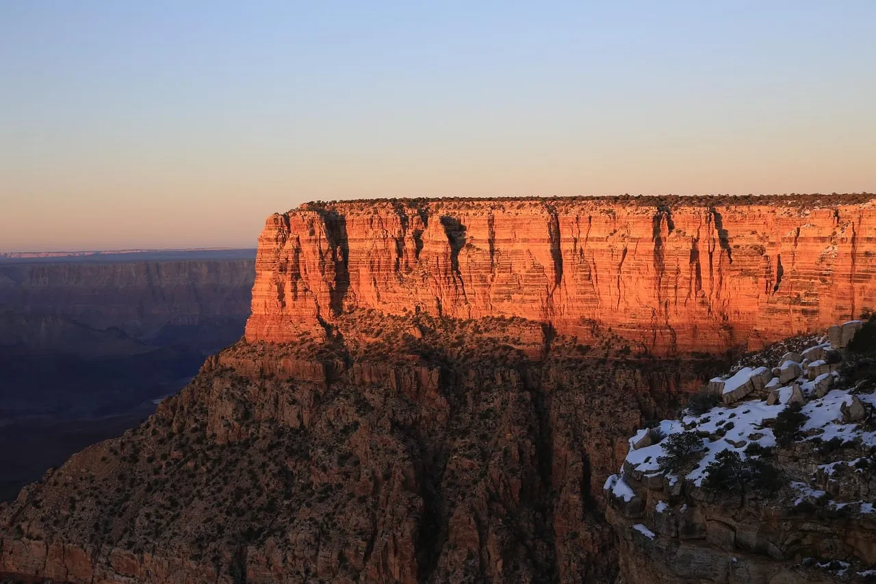 A red rock butte lit by the low sun, with snow on the rim