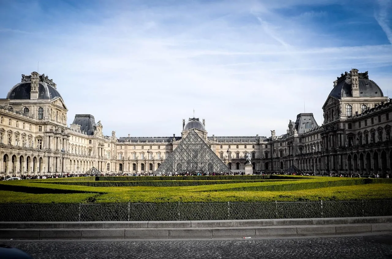The long wings of the Louvre around the pyramid, seen across a lawn