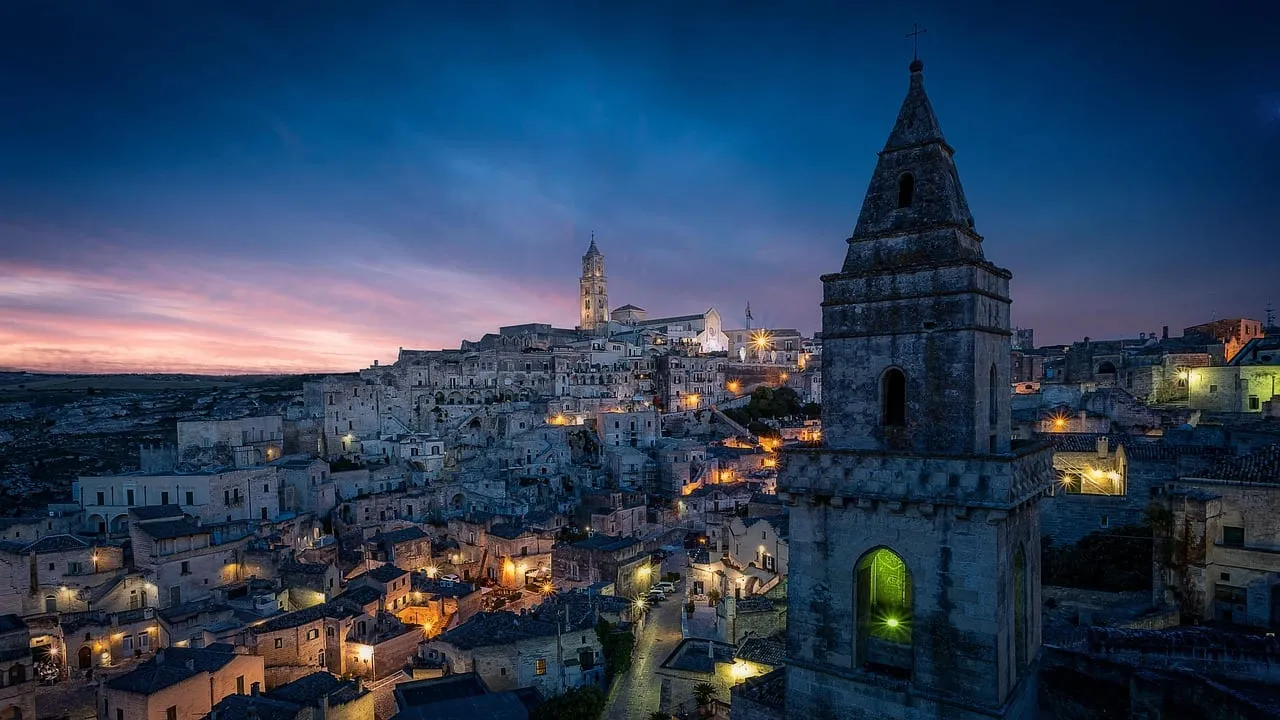 The Sassi lit up at dusk below a church bell tower