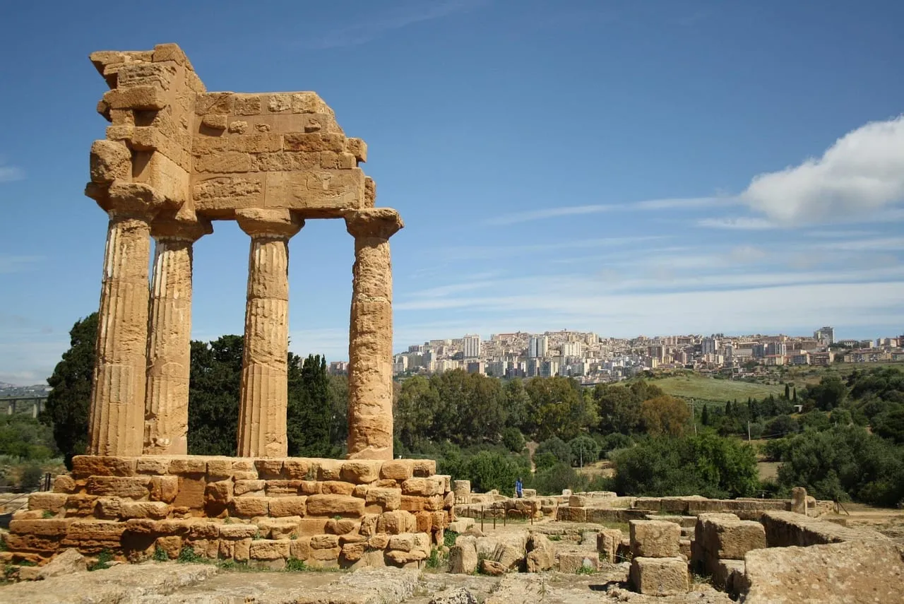 Four standing columns of a temple, with Agrigento on the hill behind