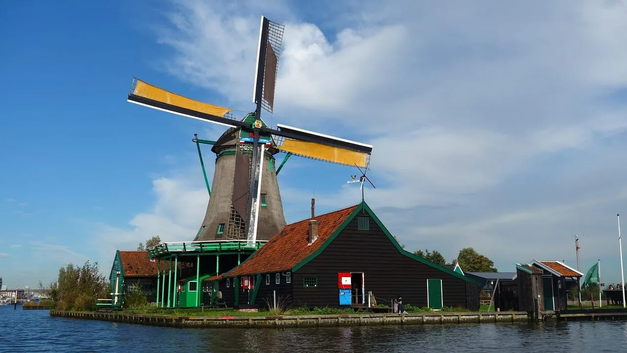 A windmill with yellow sails beside the water